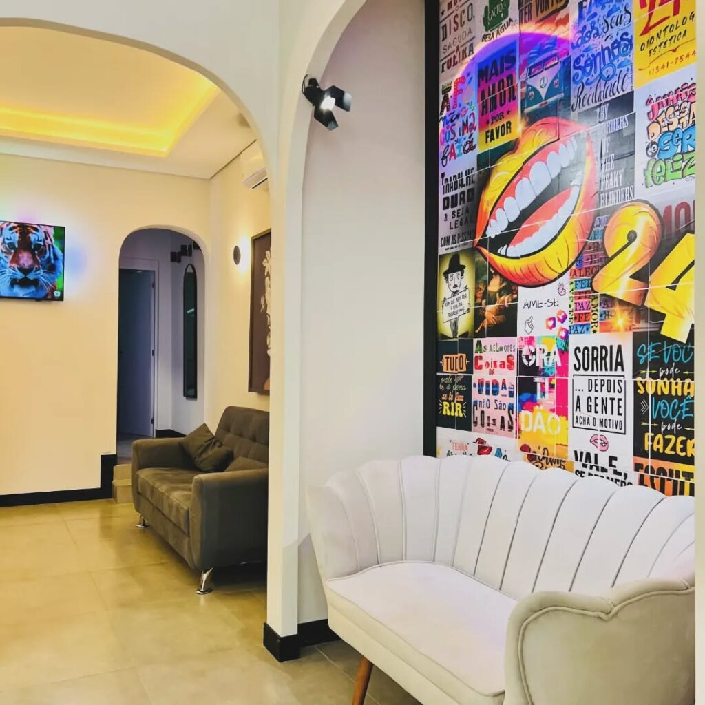 Recepção moderna e aconchegante da 24K Odontologia Estética, com sofás confortáveis, iluminação sofisticada e uma parede decorada com artes vibrantes.
